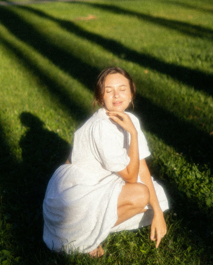Woman in a white dress sitting on grass with sunlight casting shadows