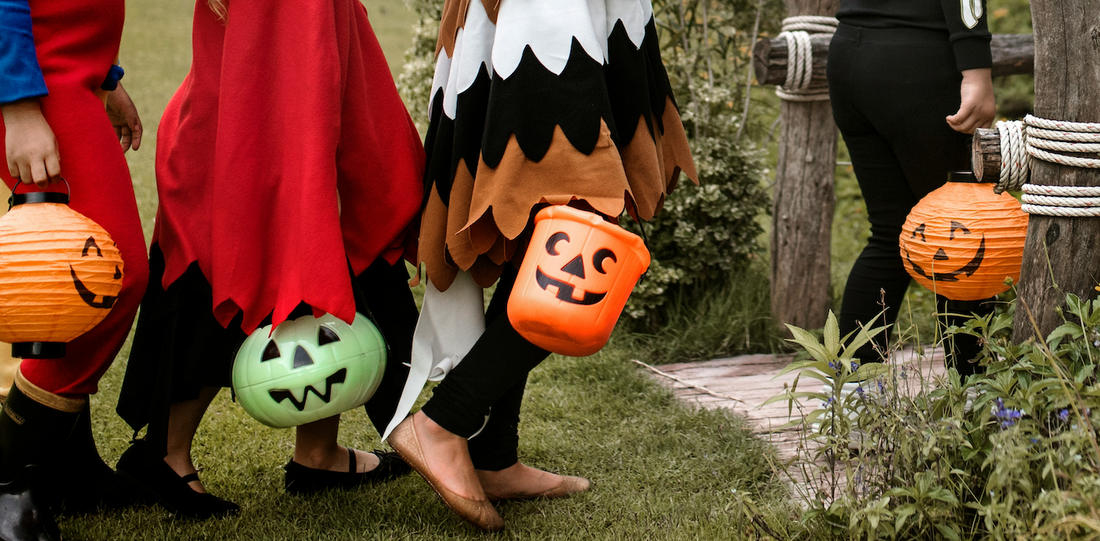 Children in Halloween costumes holding jack-o'-lantern baskets outdoors.