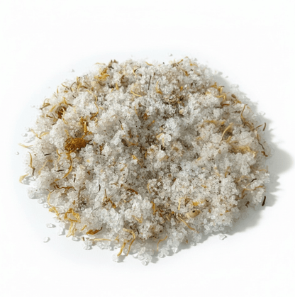 A mound of coarse white salt crystals mixed with dried yellow and brown herbal or botanical flecks, photographed on a clean white background.