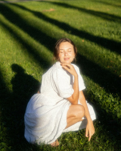 Woman in a white dress sitting on grass with sunlight casting shadows